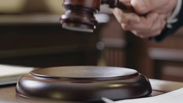 Judge's Hand Strikes Gavel on Sounding Block in Courtroom