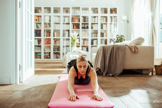 Woman practicing yoga on mat in bright living room