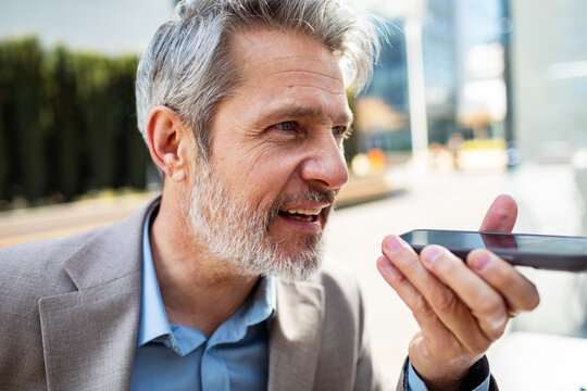 Mature businessman using voice assistant outdoors in city