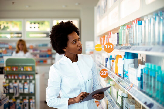 Pharmacist using tablet to check inventory in pharmacy aisle