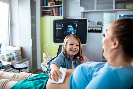 Smiling child with pregnant mother during ultrasound exam at clinic