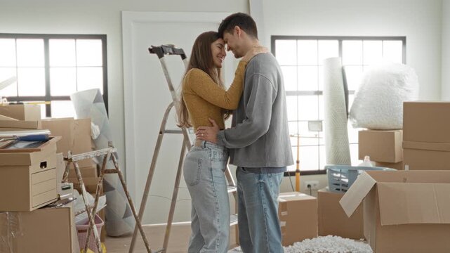 Woman embraces partner with hand on neck amid moving boxes and ladder in building; tenderness new home.