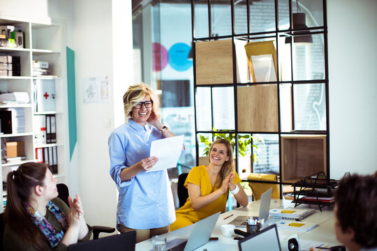 Happy coworkers applauding female leader during team meeting in modern office