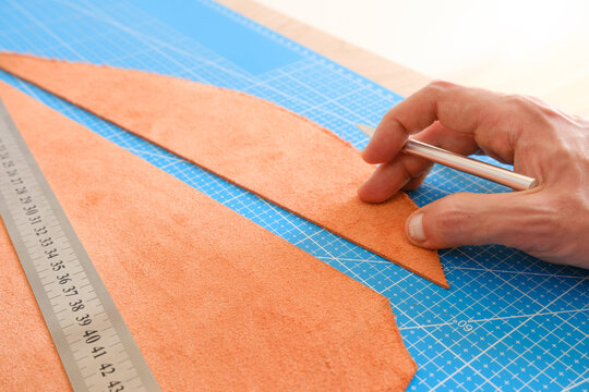 Craftsman cutting leather material with precision knife on mat