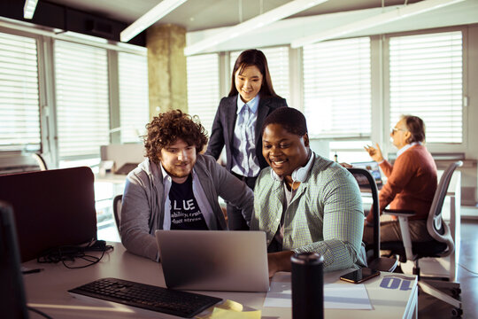 Diverse coworkers collaborating on laptop in modern open office