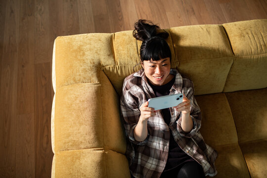 Young woman relaxing on sofa with smartphone at home