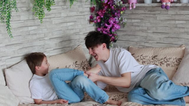Happy positive children, tickling on the feet, having fun together, boy brothers at home having wonderful day with joy