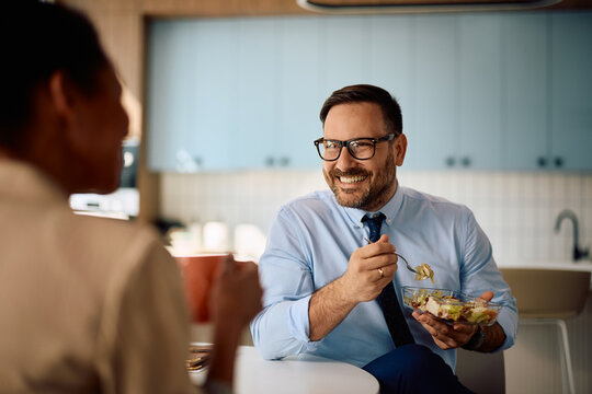 Happy entrepreneur and his colleague communicating while eating lunch in office kitchen.