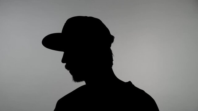 An anonymous silhouette of a man in a cap against a white wall gives an interview while hiding his identity