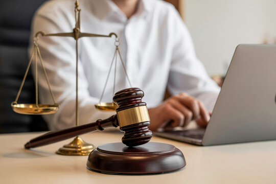Gavel and scales of justice on desk with lawyer working on laptop computer in office symbolizing legal services and law firm representation.