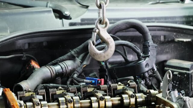 Metal hook of lift hangs over car engine section in service shop closeup. Hydraulic hoist prepares to transport heavy motor at station