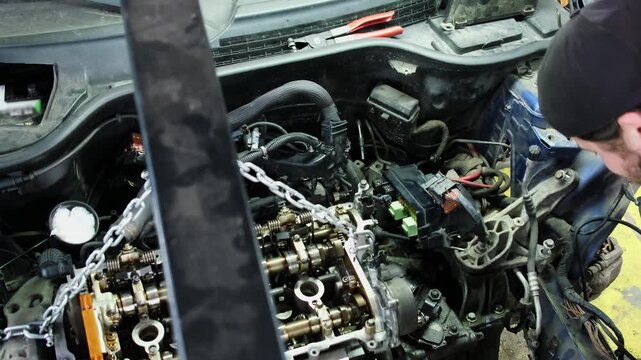 Technician hands works with car details near engine hanging on hoist in repair shop closeup. Employee fixes broken vehicle at service station
