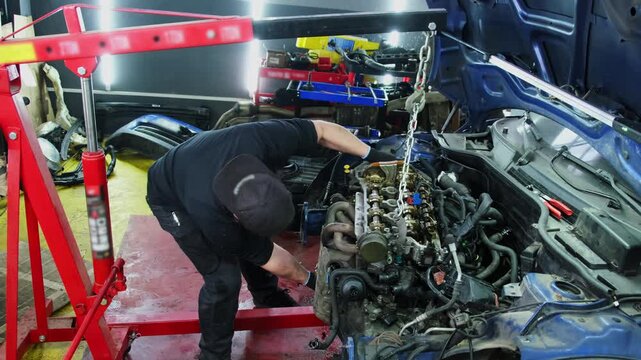 Mechanic removes car engine with hoist at repair shop slow motion. Skilled technician disconnects broken motor for maintenance in workshop