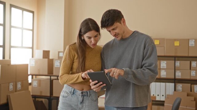 Man and woman holding tablet and smiling while checking parcels in a building; small business success joy.