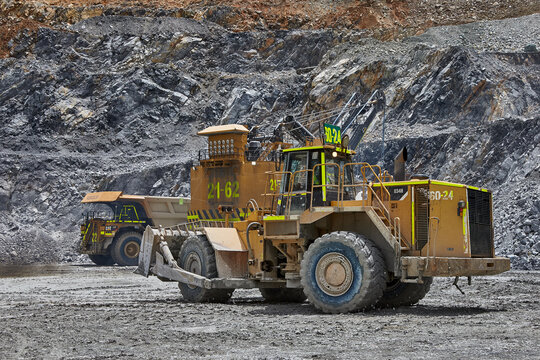 Raw power meets precision,a wheel dozer pushes through the demanding terrain of a high-altitude open pit mine under a heavy overcast sky, with a Caterpillar haul truck standing by in the background. 