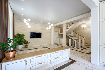 Fototapeta premium Spacious living area with light wood paneling, marble-patterned floor, white TV unit with gold handles, modern pendant lights, potted plants, open staircase with wooden railings