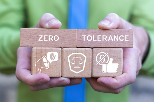 Concept of zero tolerance. Business person holding wooden blocks with icons sees the inscription ZERO TOLERANCE. Severely punishing all unacceptable behaviour.