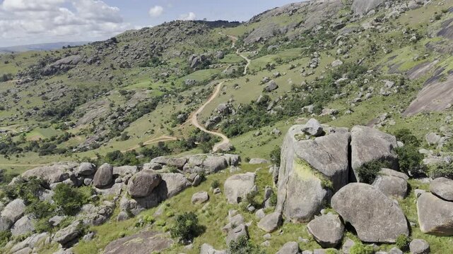 Drone flies left and pans from behind rock to reveal hiking trail below on a sunny day at Sibebe Rock near Mbabane, Eswatini