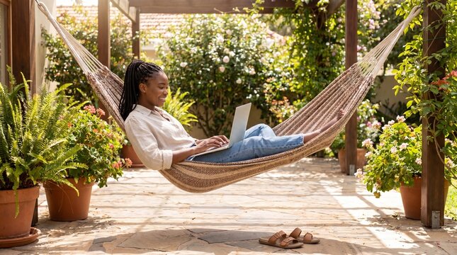 Young woman relaxing in garden hammock with laptop, smiling while working remotely amid potted plants and sunlight, peaceful outdoor workspace blending nature and productivity