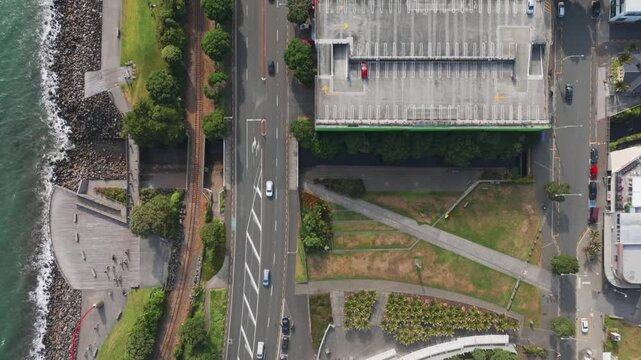 Aerial view of people cycling and walking along the waterfront promenade in New Plymouth, Taranaki, New Zealand, with traffic on the adjacent road.