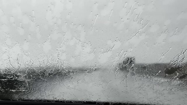 Car driving on a wet highway during a heavy downpour. Windshield wipers clearing rain from the glass, with poor visibility of the road ahead