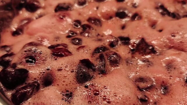Thick, sweet cherry jam or marmalade boiling and bubbling in a pot. Extreme close up shot of the homemade fruit cooking process for preservation