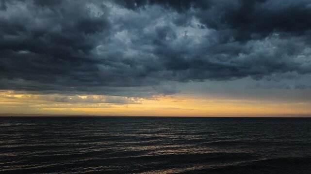 Dark, stormy clouds gathering over a restless ocean during a dramatic sunset. The ominous sky contrasts with the golden light on the horizon in Pineta, Lignano Sabbiadoro, Italy