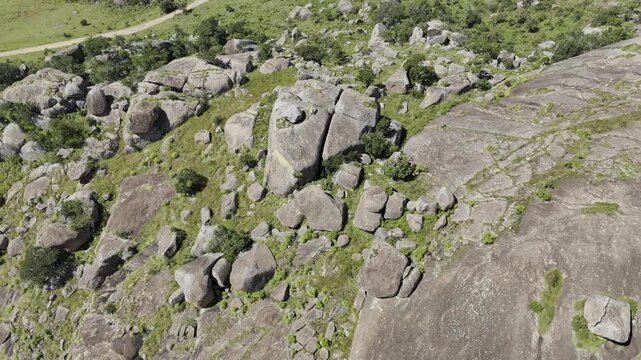 Drone lowers in bird's eye view of rocky cliffs as camera pans up to reveal hiking trail through landscape on a sunny day at Sibebe Rock near Mbabane, Eswatini