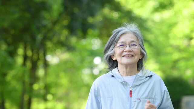 新緑の公園で運動するアクティブシニア女性の見上げる笑顔健康維持　スポーツでウォーキングやランニングのイメージ上半身のクローズアップの動画