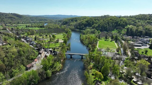 Aerial spring view of Beaulieu-sur-Dordogne France Historic village with bridge over the Dordogne River surrounded by lush green hills