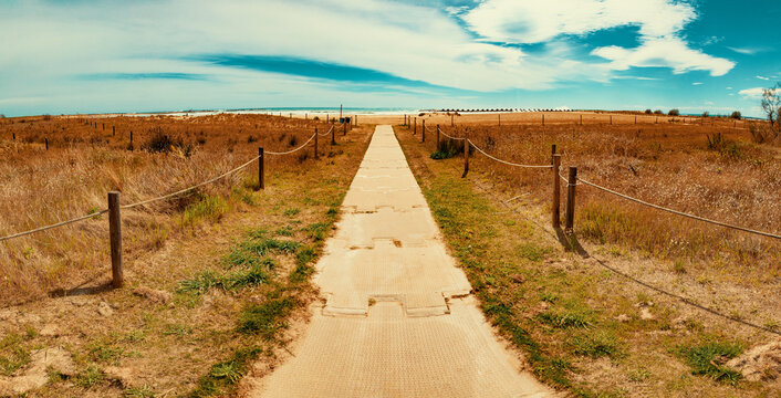 Playa de Cubelles, Catalu&ntilde;a, Espa&ntilde;a. Sendero costero que conduce al mar Mediterr&aacute;neo, evocando calma, viajes de verano, belleza natural y relax junto al mar. Pasarela de arena con postes de madera
