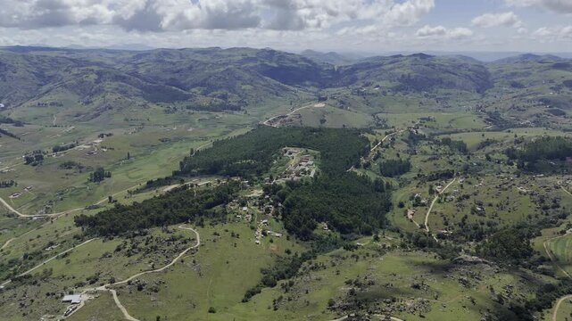 Drone flies forward and descends as it approaches a small forest on a sunny day at Sibebe Rock near Mbabane, Eswatini