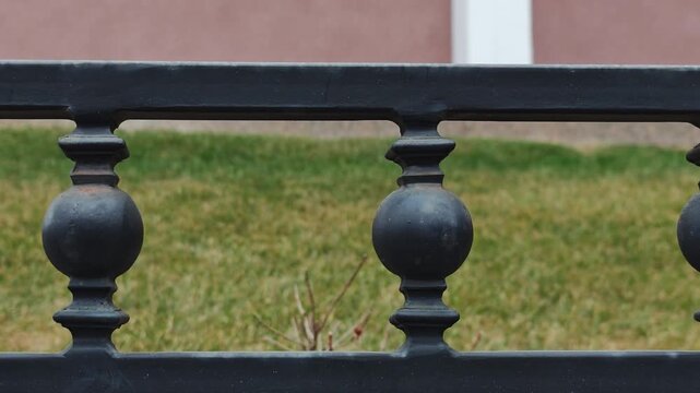 Black wrought iron fence with decorative balusters and spherical elements, showcasing a continuous view of the structure against a green lawn and pink wall background