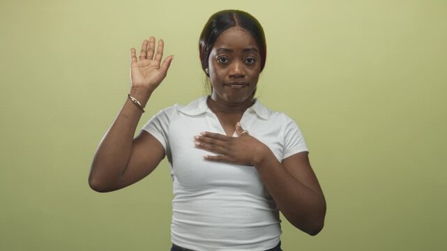 Woman with right hand raised and left hand on chest, direct gaze to camera, in studio taking an oath; commitment.
