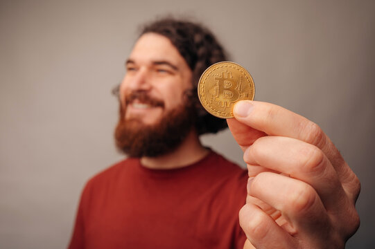 Closeup Hand Presenting Gold Bitcoin Coin With Blurred Smiling Bearded Man In Background, Crisp Studio