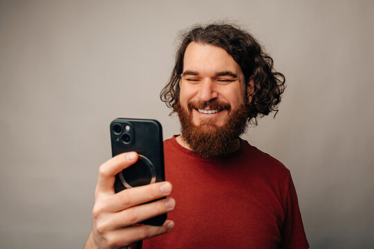 Man Looking At Phone With Warm Smile, Engaged By Message Or App Content, Casual Indoor Portrait, Modern Mobile