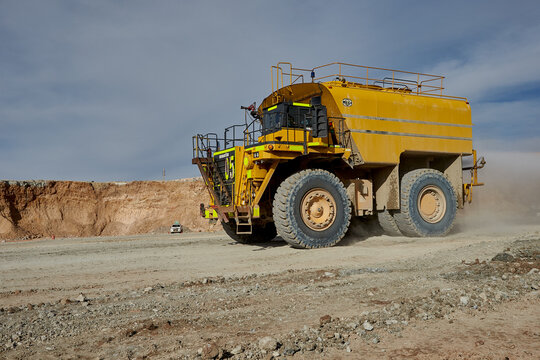A modern ultra-class water truck sprays a controlled mist across haul roads in an open-pit mine, demonstrating advanced dust suppression technology and strong environmental management. 