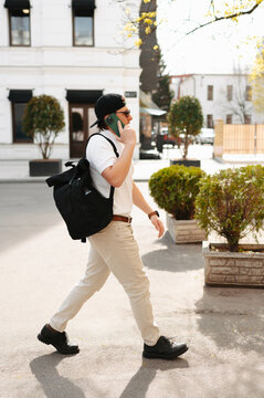 Man Walking With Backpack And Talking on smartphone, Brisk Stride Along City Sidewalk