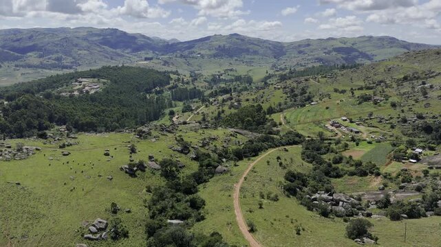 Drone lowers from wide shot of dirt hiking trail crossing the landscape on a sunny day at Sibebe Rock near Mbabane, Eswatini