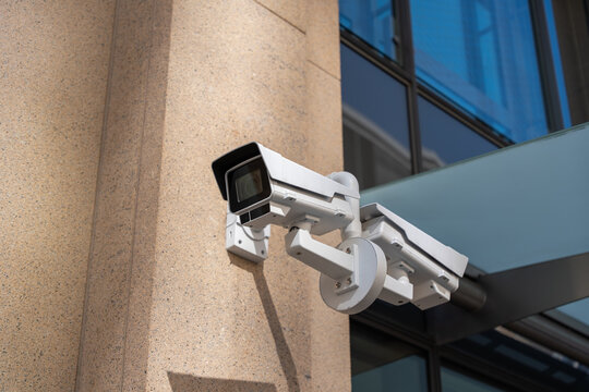 Close view of a white CCTV surveillance camera installed on a modern building facade. Urban security technology monitoring public space in Berlin city center.
