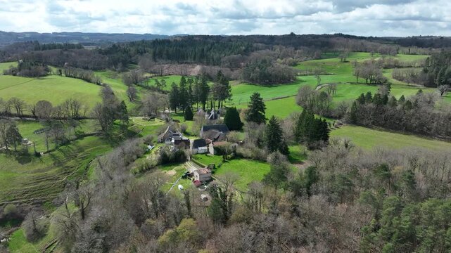 Aerial spring view of Correze France Picturesque hamlet with houses nestled in lush green fields surrounded by rolling hills and dense forests