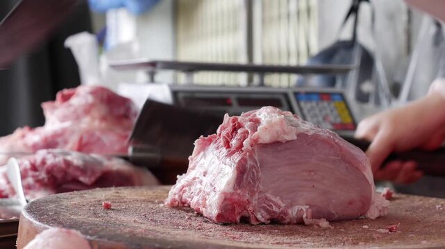 Butcher forcefully chops meat with bone using a cleaver on a round wooden chopping block while preparing raw portions for sale at a traditional market stall. Butcher work.