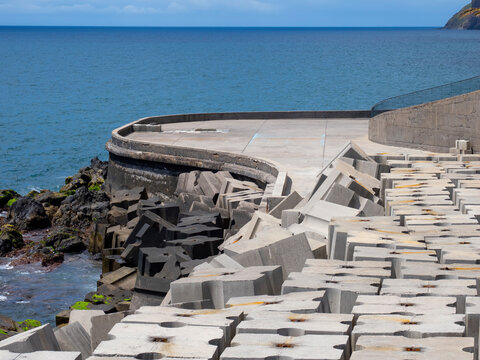 Coastal protection structure made of heavy concrete modules along the shoreline with wave breakers and rugged rocky coast at the ocean (Madeira)