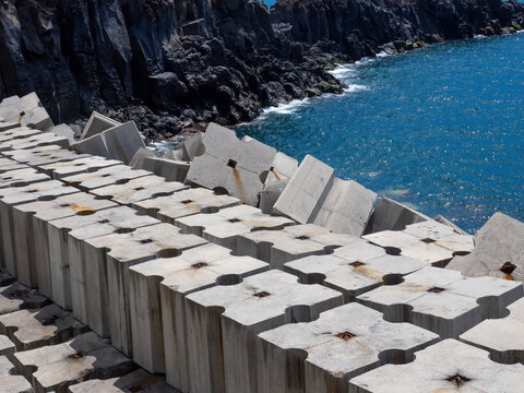 Coastal protection structure made of heavy concrete modules along the shoreline with wave breakers and rugged rocky coast at the ocean (Madeira)