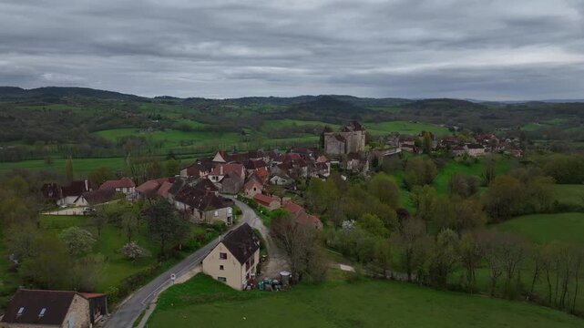 Aerial view of Curemonte France with Saint Hilaire castle overlooking the historic village nestled in lush green rolling hills under cloudy sky