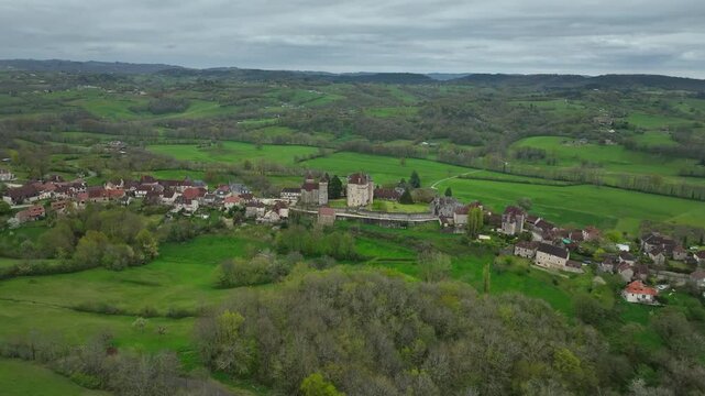 Aerial view of Curemonte France with Saint Hilaire castle and historic village nestled in lush green rolling hills under cloudy sky