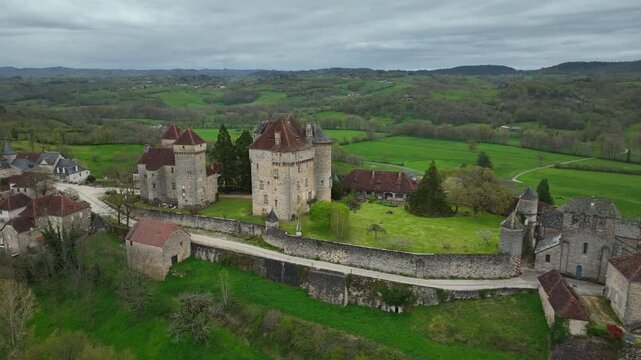 Aerial view of Curemonte France with Saint Hilaire castle and historic stone buildings overlooking lush green countryside under cloudy sky
