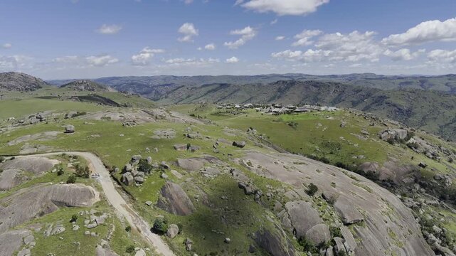 Drone lowers from wide shot of entire landscape down to a lone hiker climbing a trail on a sunny day at Sibebe Rock near Mbabane, Eswatini