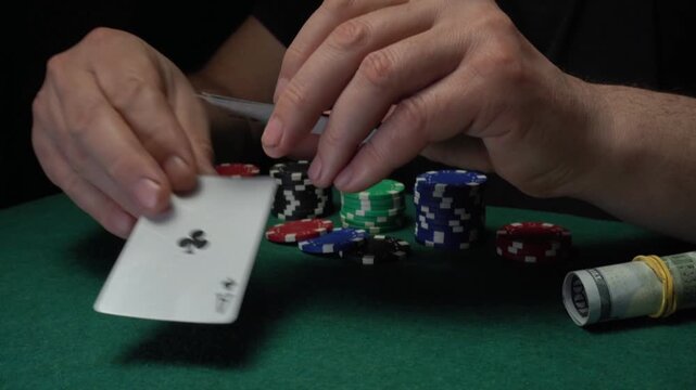 Male poker player's hands holding playing cards, showing three aces or set, surrounded by colorful poker chips and cash on a green felt table