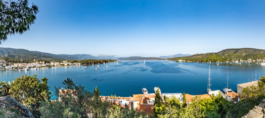 Naklejka premium Panoramic view of Poros town and marina in Poros, Greece, with sailboats on a calm blue bay, green hills, and clear sky, ideal for travel and vacation concepts
